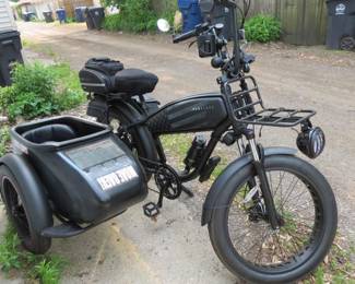 black electric "mud bike" with a sidecar, equipped with storage bags and a basket