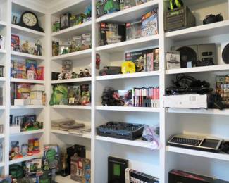 A display room of pop culture collectibles, featuring LEGO sets, action figures, retro games, DJ Hero gear, and vintage electronics.....