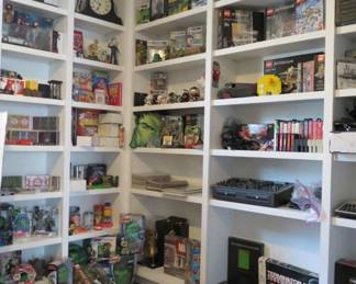 A display room of pop culture collectibles, featuring LEGO sets, action figures, retro games, DJ Hero gear, and vintage electronics......