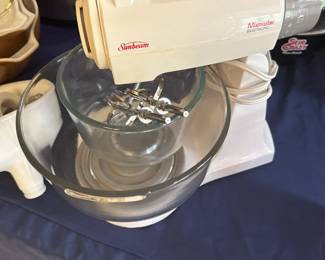 Sunbeam Mixmaster Electronic Stand Mixer,
A classic and well-known kitchen tool that has been a household staple for decades.
🧁 About This Model
Brand: Sunbeam
Model Line: Mixmaster Electronic
Era: Likely from the 1980s to the early 1990s
Features:
Two glass mixing bowls
Beaters and possibly dough hooks (if all accessories are intact)
Detachable hand mixer component (dual-function as a stand and hand mixer)
Multiple speeds (you can see the numbered dial on the side for various mixing tasks)
Rotating turntable base for bowl movement during mixing
Sunbeam Mixmasters were renowned for their durability and simplicity, making them versatile for a wide range of tasks, from whipping cream to kneading dough.
Collectors and vintage kitchen enthusiasts appreciate these for both practical use and retro charm.