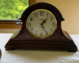 Howard Miller Marquis Mantel Clock 635-115 This tambour-style timepiece blends traditional craftsmanship with modern functionality. Finished in Windsor Cherry on select hardwoods and veneers, it features a decorative inlay pattern of multiple hardwoods, an arched molding crowning the case, and carved wood molding wrapping around the front and sides. The white dial showcases black Arabic numerals and serpentine hour and minute hands, framed by a polished brass-tone bezel and convex glass crystal. This clock operates on a quartz, dual-chime movement, offering Westminster or Ave Maria chimes, volume control, and an automatic nighttime chime shut-off option. Its dimensions are approximately 11.5 inches in height, 18.25 inches in width, and 7 inches in depth .