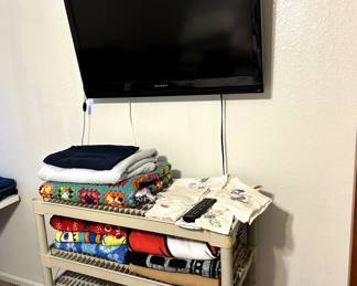 TV with Antenna and remote, blanket crocheted by Aunt Biddy (1960s), cloths cross stiched by family and friends (1940s -70s)