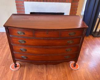 Price: $325
Classic Dixie Furniture bow front dresser in traditional Federal style, featuring fluted legs, carved rosettes, and original brass oval hardware. The deep mahogany finish and elegant curved front give this piece timeless appeal.
Structurally excellent, with drawers that glide smoothly. Top surface has visible scratches and watermarks, but overall presentation is strong. A beautiful candidate for restoration or use as-is in a traditional or eclectic interior.