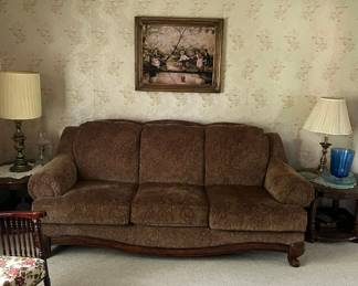 Traditional upholstered sofa with brown paisley fabric, carved wood trim, and rolled arms.
Wall art in ornate gold frame.
Classic brass table lamp with pleated shade.
Round wood side table with marble top and decorative legs.