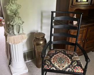 Decorative ceramic statue of seated girl on fluted pedestal column.
Large vintage brass vase with patina finish.
Black wood armchair with ladder back and upholstered seat in ornate tapestry fabric.