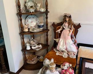 Five-tier corner whatnot shelf with turned wood supports. Vintage porcelain pitchers, teacups, and decorative dishware.
Victorian-style porcelain dolls with detailed gowns and bonnets.
Upholstered side chair with carved wood back and mustard velvet seat.