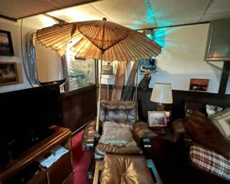 Leather lounge chair and ottoman set with tufted cushions, and a wooden side table and lamp. a large, decorative paper parasol umbrella. Wooden TV stand.