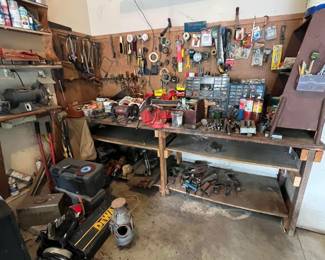 Workshop corner with a wooden workbench covered in tools, supplies, and parts.
Pegboard wall above the bench with organized hand tools, measuring tapes, tape rolls, and small hardware in drawers and bins.
Workbench shelves underneath holding more tools and equipment.