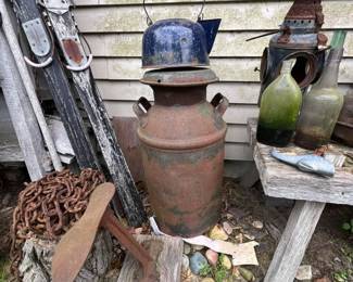 Rusty vintage milk can with lid.
Blue speckled enamelware kettle.
Cast iron anchor with heavy chain.
Old green glass bottles and ceramic jug.
Rusty lantern frame and tin oil can.
Pair of antique wooden skis with metal bindings.
Hand-carved wooden fish decoy.