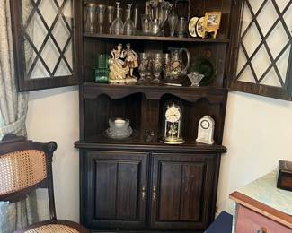 Vintage dark wood corner hutch with display shelves and storage cabinet. Also pictured: assorted crystal glassware, porcelain figurines, vintage mantel clocks, and decorative collectibles. Great for traditional or antique-style interiors.