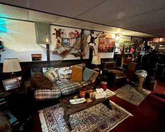 Plaid fabric sofa with assorted throw pillows, leather armchair, wooden coffee table on a decorative area rug. Decor includes mounted nautical wall art, lamps, and much more