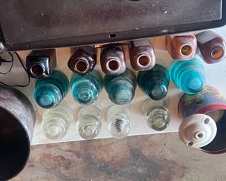 Located in the garage. This table has 6 snuff bottles, 5 blue powerline insulators, 4 clear glass powerline insulators, and a tin with 5 of the white ceiling insulators.