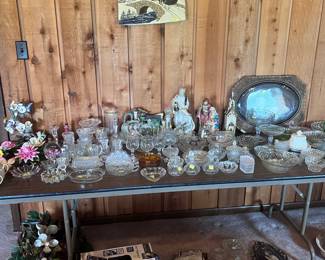 This table is located on the left side of the living room area. It has several porcelain flowers, pieces of lead crystal, a variety of vintage bowels, candy dishes, and serving trays. In addition, there are two large Mary and Joseph figures and a very old photograph. Be sure to look on the floor under the tables as well. This table has a miniature Shark vacuum and several other items.
