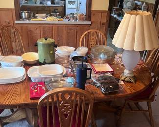 This is located in the dining area. The oak dining table and chairs are for sale. On the table are pieces of Blue Cornflower Corning Ware with lids, a vintage green coffee maker, several pieces of Pyrex, and other glass mixing bowls.