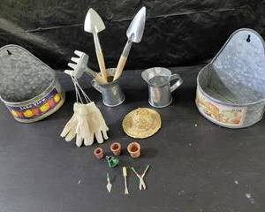 Several pieces of toy gardening tools, gloves, rack, shovel, hoe, gloves, watering pitcher, tool holder, and small planter container for the young gardener or for a store display.