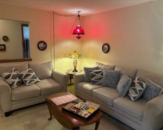 Tan/light neutral, heathered colored couch and loveseat with decorative blue pillows. Coffee table. Tiffany style lamp, hanging cranberry lamp.