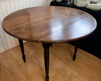 R20 - $125 - Round Wood Drop Leaf Dining Table. Chairs not included. The table is in great condition! With natural wood finish on top and black painted legs. Measures 42" round and 26"W when dropped.