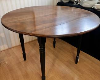 R20 - $125 - Round Wood Drop Leaf Dining Table. Chairs not included. The table is in great condition! With natural wood finish on top and black painted legs. Measures 42" round and 26"W when dropped.