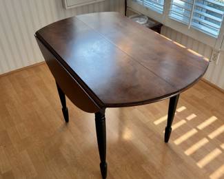 R20 - $125 - Round Wood Drop Leaf Dining Table. Chairs not included. The table is in great condition! With natural wood finish on top and black painted legs. Measures 42" round and 26"W when dropped.