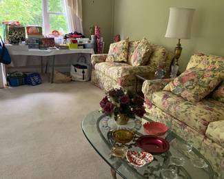 Floral upholstered sofa and loveseat. Ornate glass coffee table, long table full of holiday gift wrap and a few misc. ashtrays on the coffee table.