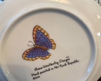 Anna Weatherley Designs™, a luxury porcelain line known for its hand-painted tableware. The marking on the bottom indicates:
Hand painted in the Czech Republic
Dated 2003
The design features a colorful butterfly, characteristic of Anna Weatherley’s botanical and insect-themed patterns.
