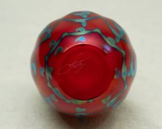 Closeup of a Charles Lotton art glass vase, zipper design of pulled blue green over red ground, crimped rim; engraved signature to base.
