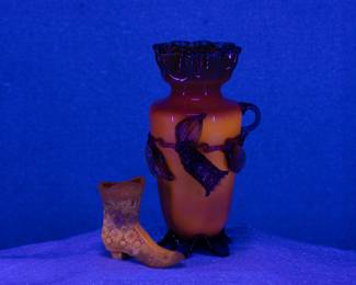 Seen under blacklight: Antique Stevens & Williams art glass vase, opaque yellow glass with applied clear green rigaree glass leaves and blossoms, ruffled edge and tabbed feet, the body with uranium glass that glows under black light. Also shown a Fenton EAPG canary yellow milk glass Daisy & Button design ladies' shoe or boot, uranium glass.