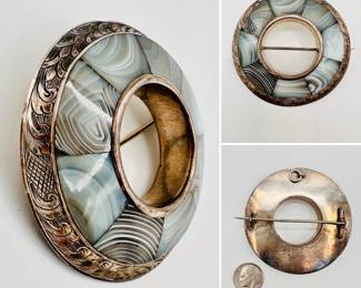 A early to mid-19th century Scottish sterling silver banded agate pebble brooch pin. Striped and figured grey and white banded agate fitted stones held in a finely hand engraved decorated outer rim. Original c-clasp and a loop for a safety chain and safety pin. Typically unsigned with no hallmarks and it would have been worn as a garter, kilt or sash pin.