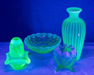 Photographed under black light: Fenton Glass three piece green opalescent uranium glass Fern pattern fairy lamp, a Fenton Honeycomb and Clover green opalescent uranium glass bowl, a Fenton opalescent ribbed green uranium glass vase, and an EAPG Dugan Palm and Scroll green opalescent rose bowl, uranium glass.