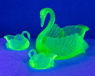 Under black light, the vintage Cambridge vaseline glass or green uranium glass swan punch bowl, with two small matching swan shape cups. The cups marked to the base with the letter "C" in a triangle; the set dates to the 1930s.