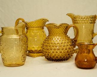 An Anchor Hocking Springsong Honey Gold glass pitcher, a vintage amber glass coin dot or polka dot pircher with applied twisted handle, an antique Hobbs Brockunier amber glass Dewdrop Hobnail pitcher EAPG, antique Adams & Co. Amber Wild Flowers glass pitcher late 19th Century, and a small brown or amber crackle glass pitcher or creamer with applied smooth handle