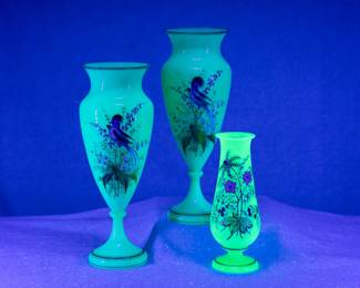 Seen under UV light: A beautiful pair of vintage uranium glass opaline vases in robin's egg blue, hand painted with birds and flowers with gilt accents, and a smaller opaline green uranium glass vase hand painted with flowers and gilt accents. All three are likely Bohemian art glass by Harrach late 1880s.