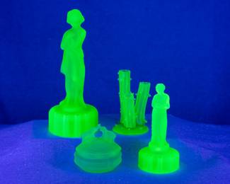 Seen under UV light: A vintage Cambridge Glass 'Draped Lady' flower frog, an Art Deco classic in satin finish emerald green uranium glass; a Steuben Glass 'Triple Stump' bud vase (shape 2744 designed by Frederick Carder) in Jade green uranium glass, a 1930s Art Deco 'Kissing Elephants' powder jar or trinket dish in green frosted uranium glass by L.E. Smith, and a Cambridge uranium glass 'Rose Lady' flower frog.