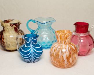 Art glass pitchers including marbled pattern amber, cranberry glass with clear glass applied handle, a Nailsea blue glass pitcher with white pulled lines