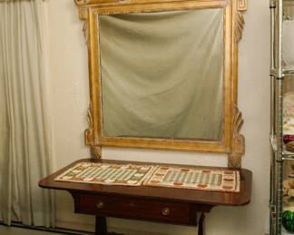 Large vintage gilt wood mirror with stylized farm or harvest design at the top - floral basket, a shovel and rake crossed behind, and flowing sprays of leaves.