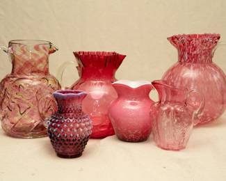 Ann antique Northwood Glass Company No. 287 / Royal Ivy water pitcher, colorless with cranberry and yellow spatter; a Fenton cranberry opalescent hobnail syrup pitcher, a cranberry glass coin dot or thumbprint pitcher with applied clear handle and ruffled rim, a red and white cased glass spattered vase, a small pale cranberry glass/pink glass ribbed vase with applied clear handle, and a Northwood Cranberry opal spatter water pitcher with square crimped rim, clear applied handle