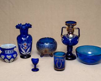 A Bohemian glass blue and opalescent white cut to clear pitcher or creamer; Antique Fenton 'Garland' pattern blue carnival glass three-toed rose bowl; a (likely Bohemaian glass) hand-painted and gilt double handled cobalt blue amphora style vase with a tall stem and flared foot; a vintage 1940s cobalt blue glass eye wash cup – the pedestal and sides of the cup of octagonal design; a small Portieux Vallerysthal cobalt blue glass with gilt decoration of floral swags, and a clear cobalt blue glass bowl