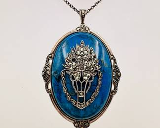 Closeup of the pendant from the delicate sterling silver link necklace with blue stone pendant decorated with a silver filigree and marcasite flower basket.. Marked to the back with "Sterl. Silv." and artisan's stamp.
