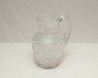 A Peleton glass pitcher, handblown colorless glass pitcher with textured exterior and applied threaded design in pink, white, yellow, and blue.