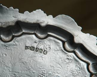 Closeup of the 18th century sterling silver salver, center decorated with a coat of arms inside a wide band of floral and water plants with swimming ducks; English hallmarks