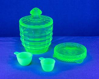 Seen under blacklight: Vintage Anchor Hocking Block Optic green uranium glass candy dish & lid circa 1929-1933, depression glass; a vintage green uranium glass / vaseline glass dish with raised edges, and two vintage Jeanette Glass Jadeite uranium glass tab-handled measuring cups
