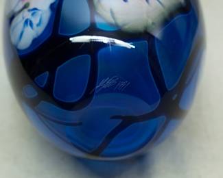 Closeup of the original hand blown art glass by John Lotton, in rich blue cased glass with pink and white heart shaped flowers and dark vines, iridized flared rim. Signed John Lotton 1991.