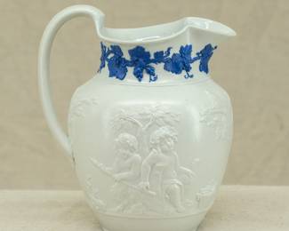 Another view of the antique Wedgwood "Bacchanalian Boys" pitcher, white jasper, decorated with Classical imagery of young boys and satyrs in Bacchic revelry (with grapes and grape leaves in their hair.) On one side, a young Bacchus holding his thyrsus (fennel staff) is being held aloft by two other boys, a vessel of wine beside them; the other scene has a satyr and a boy sitting beneath a tree. The neck of the pitcher has applied blue sprig band of fruiting grape vines. Marked with "WEDGWOOD" to the base, dating 1790 to 1820. The design is based on drawings sent to Josiah Wedgwood by artist Lady Diana Beauclerk, née Spencer (1734-1808), daughter of the 3rd Duke of Marlborough.