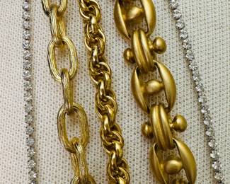 Closeup of the beautiful costume jewelry necklaces in various lengths including a gold star and black stone pendant on a gold link chain (Erwin Pearl), a long gold chain knotted in lariat style (Marshall Field), and two different length round-cut rhinestone chain necklaces (Les Bernard)