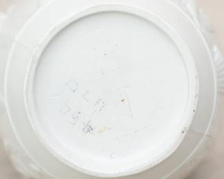 Closeup of the antique Wedgwood "Bacchanalian Boys" pitcher, white jasper, decorated with Classical imagery of young boys and satyrs in Bacchic revelry (with grapes and grape leaves in their hair.) On one side, a young Bacchus holding his thyrsus (fennel staff) is being held aloft by two other boys, a vessel of wine beside them; the other scene has a satyr and a boy sitting beneath a tree. The neck of the pitcher with applied blue sprig band of fruiting grape vines. Marked with "WEDGWOOD" to the base, dating 1790 to 1820. The design is based on drawings sent to Josiah Wedgwood by artist Lady Diana Beauclerk, née Spencer (1734-1808), daughter of the 3rd Duke of Marlborough.