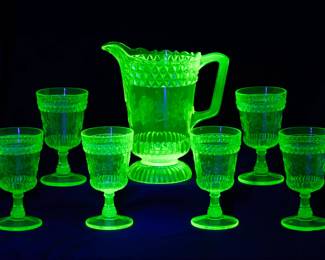 Under black light: A U.S. Glass Co. Wildflower pattern vaseline / uranium glass seven-piece water or lemonade set comprising a water pitcher and six tumblers, fourth quarter 19th century.