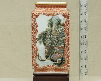 A Chinese rectangular vase dating from the 1950s with wooden stand. Vase features a coral red lotus and flower tracery ground and 2 famille rose landscape scenes on the front and back. The bottom of the vase has a 4-character mark. 