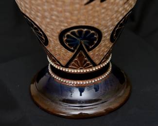 Closeup of the massive antique Royal Doulton Lambeth stoneware baluster vase, 18-1/2 inches tall. Decorated with a graceful spray of flowers over a textured pale amber ground between a band of deep blue and brown lappets and roundels at the shoulder and points with roundels at the foot, a collar of white beaded overlapping blue roundels on the neck, two bands of white beading above the foot. Base with impressed Doulton Lambeth mark, artist's marks, and model numbers. Late 19th century.
