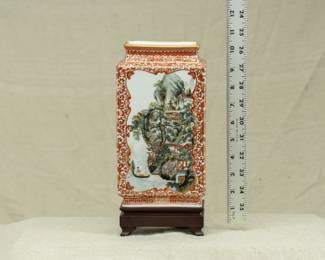 A Chinese rectangular vase dating from the 1950s with wooden stand. Vase features a coral red lotus and flower tracery ground and 2 famille rose landscape scenes on the front and back. The bottom of the vase has a 4-character mark. 