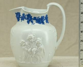 Antique Wedgwood "Bacchanalian Boys" pitcher, white jasper, decorated with Classical imagery of young boys and satyrs in Bacchic revelry (with grapes and grape leaves in their hair.) On one side, a young Bacchus holding his thyrsus (fennel staff) is being held aloft by two other boys, a vessel of wine beside them; the other scene has a satyr and young Bacchus sitting beneath a tree. The neck of the pitcher has applied blue sprig band of fruiting grape vines. Marked with "WEDGWOOD" to the base, dating 1790 to 1820.  The design is based on drawings sent to Josiah Wedgwood by artist Lady Diana Beauclerk, née Spencer (1734-1808), daughter of the 3rd Duke of Marlborough.